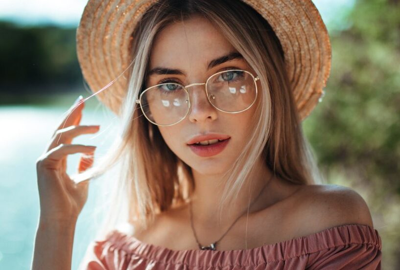 A woman wearing glasses and a straw hat, gazing directly at the camera - San Dimas Optometry A woman wearing glasses and a straw hat, gazing directly at the camera - San Dimas Optometry