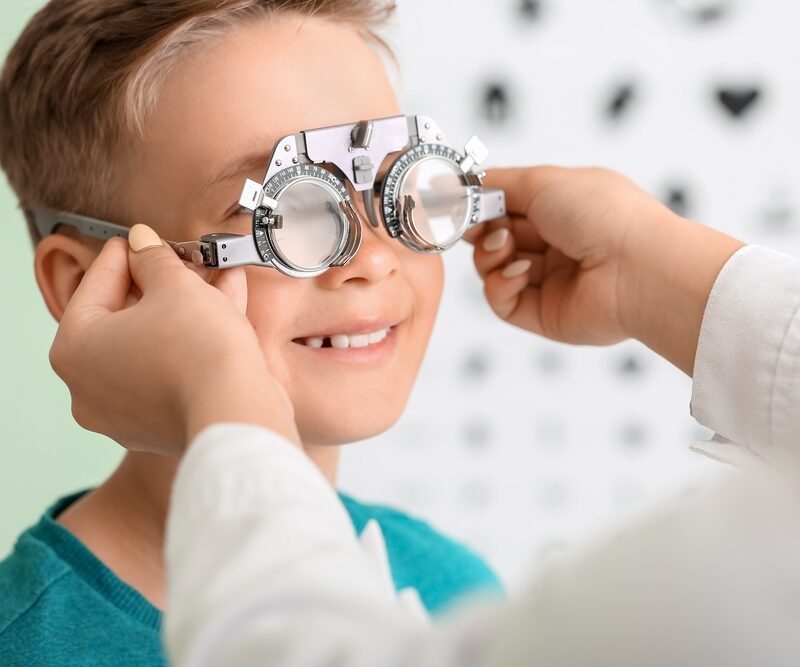 A child smiles while undergoing an eye examination with a trial frame at an optometrist's office - Eye allergy treatment