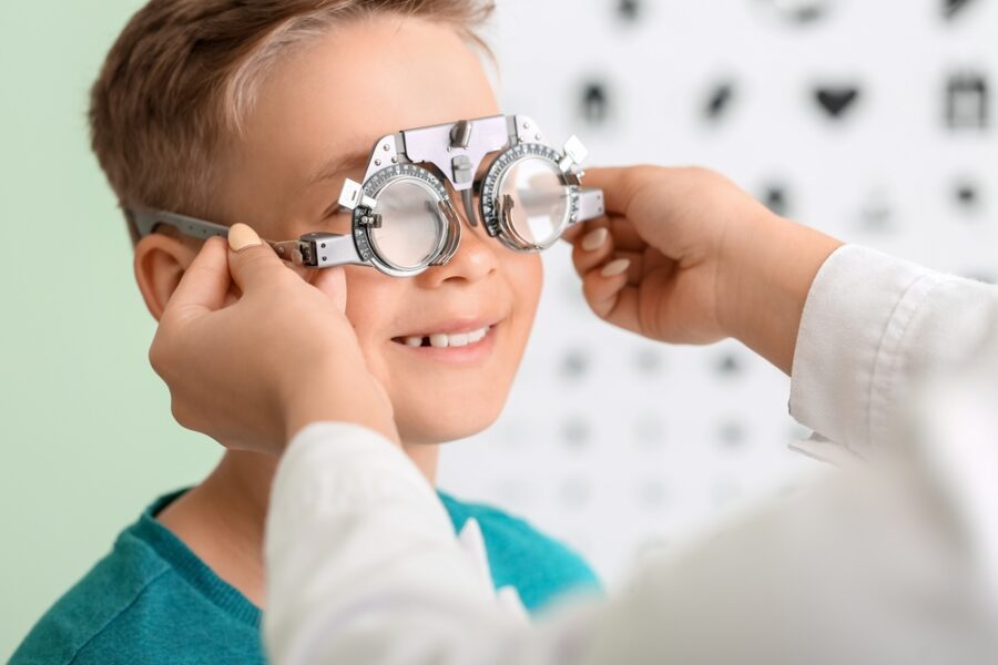 A child smiles while undergoing an eye examination with a trial frame at an optometrist's office - Eye allergy treatment
