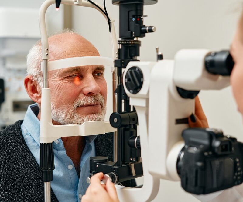 An elderly man undergoes an eye examination using a slit lamp machine - Glaucoma treatment