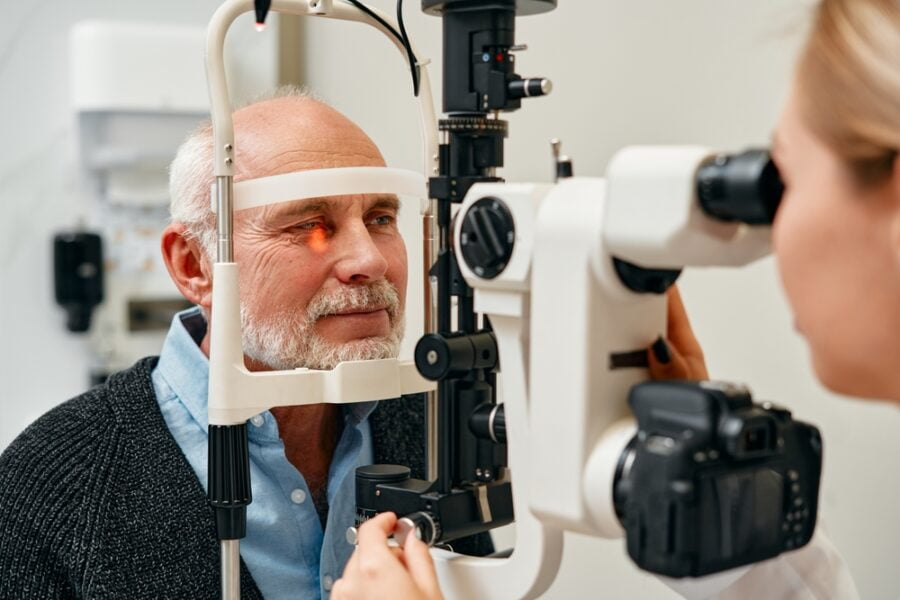 An elderly man undergoes an eye examination using a slit lamp machine - Glaucoma treatment