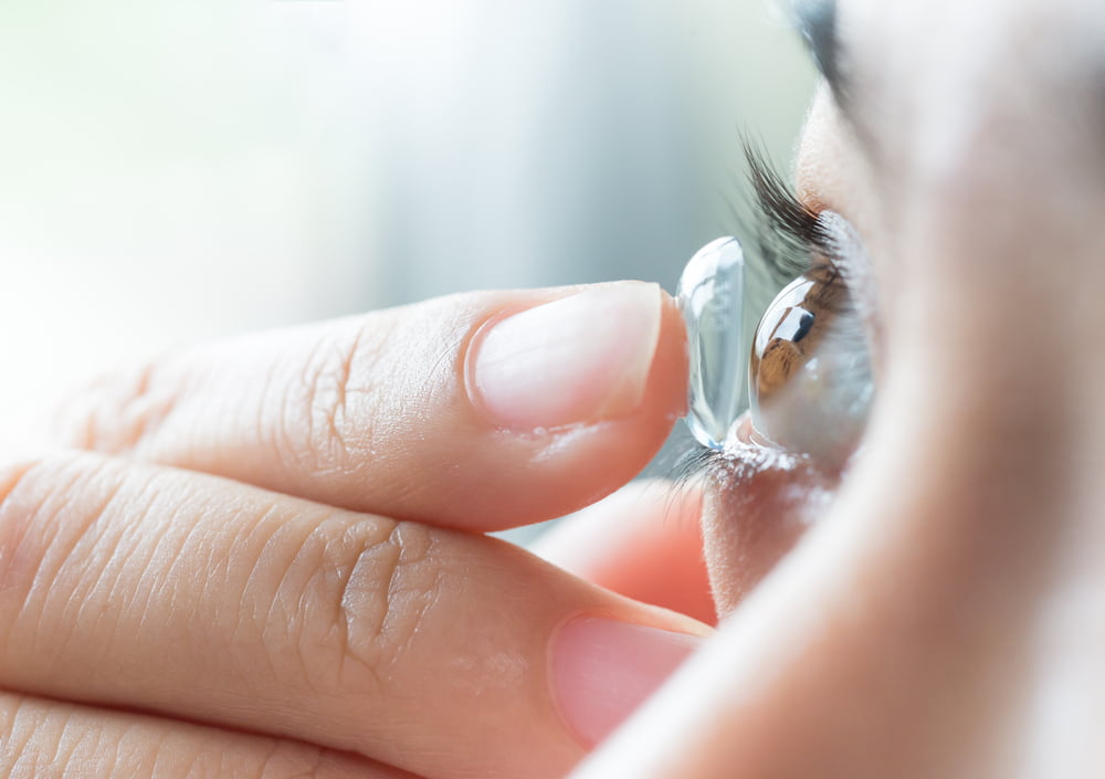 A close-up of a person inserting a contact lens into their eye, with a clear focus on the lens and their eyelashes - hard to fit contacts A close-up of a person inserting a contact lens into their eye, with a clear focus on the lens and their eyelashes - hard to fit contacts