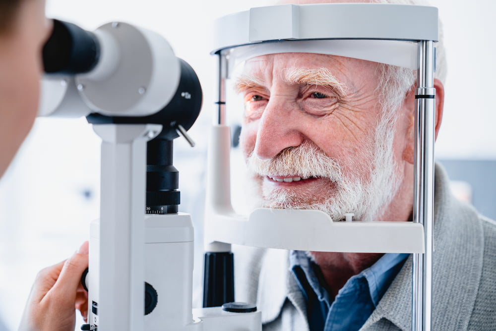 An elderly man smiling while undergoing an eye examination with a slit lamp machine during a routine check-up - Glaucoma Treatment An elderly man smiling while undergoing an eye examination with a slit lamp machine during a routine check-up - Glaucoma Treatment
