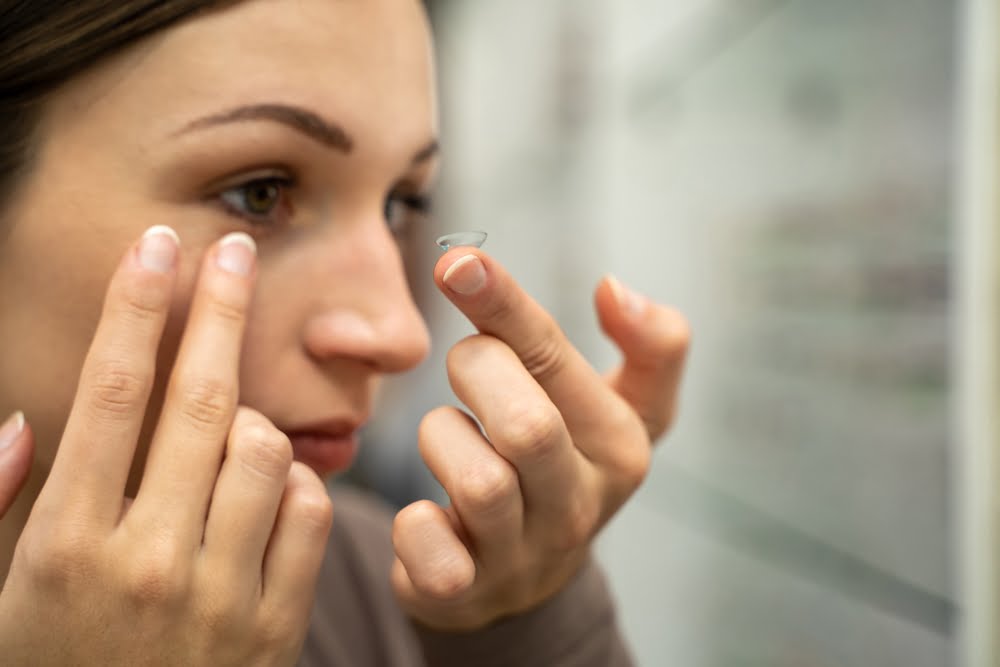 A close-up of a woman carefully inserting a contact lens into her eye - contact lens exam A close-up of a woman carefully inserting a contact lens into her eye - contact lens exam