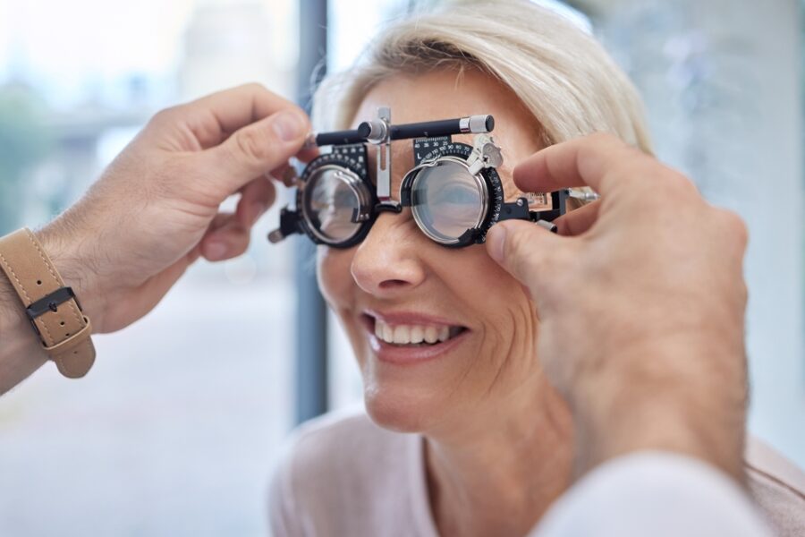 A smiling woman undergoing an eye exam as an optometrist adjusts the lenses on a trial frame - Eye & Vision Exams